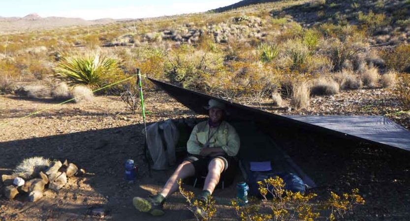 a person sits under a tarp shelter in the desert on an expedition with outward bound